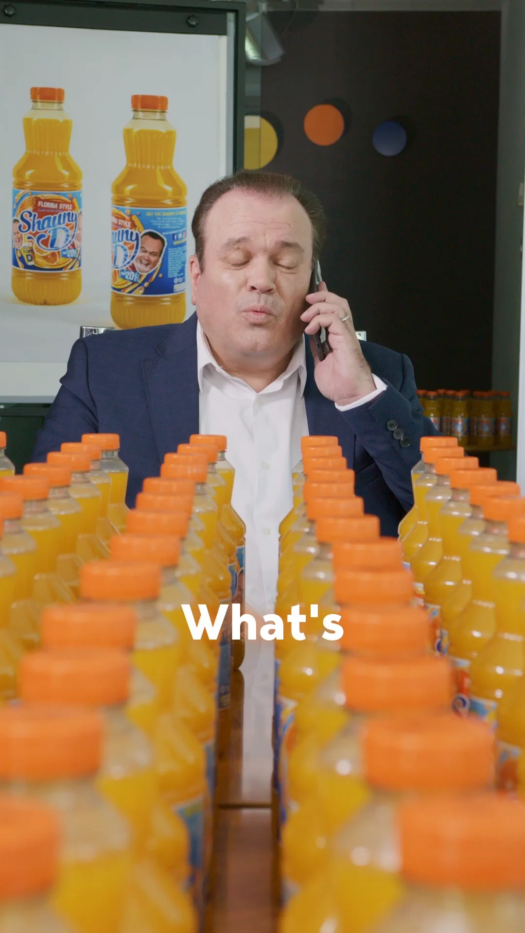 A person talking on a cell phone in front of a row of orange juice bottles